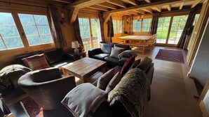 Ein gemütliches Blockhaus-Interieur mit einem Holzesstisch, Ledersofas und Blick auf einen Wald durch große Fenster.