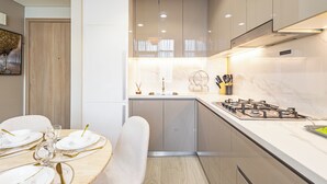A modern kitchen with a central island, built-in appliances, and a dining area with a table set for four. - Superhost Modern 1BR in Azizi Riviera (Dubai)