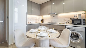 A modern kitchen with a dining area, featuring a round table set for four, a built-in oven, and a washing machine. - Superhost Modern 1BR in Azizi Riviera (Dubai)