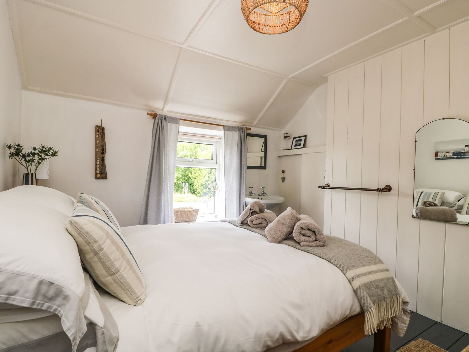 A bedroom with a large bed, a window with curtains, a bedside table with a lamp, and a mirror on the wall.