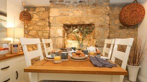 Un ambiente para el desayuno con chimenea de piedra, mesa de madera, sillas blancas y diversas opciones para el desayuno.
