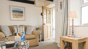 Una sala de estar acogedora con un sofá color beige, una mesa de centro con una cesta, una lámpara y un cuadro en la pared.