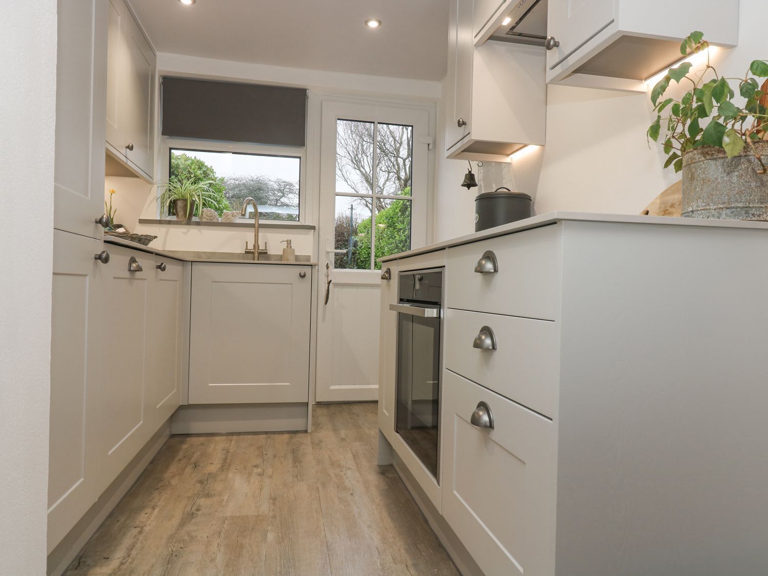 A modern kitchen with white cabinetry, a built-in oven, and a window with a view of greenery.