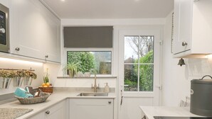 Una cocina moderna con armarios blancos, horno empotrado y ventana con vistas al verdor.