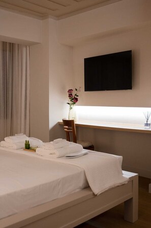 Ein Hotelzimmer mit Bett, Schreibtisch, Stuhl, Fernseher und einem Fenster mit Vorhängen.