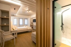 Ein Hotelzimmer mit Bett, Sessel, kleinem Tisch, Duschkabine aus Glas und Wandpaneelen aus Holz.