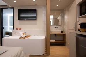 A modern bathroom with a freestanding bathtub, a large mirror, and a flat-screen TV mounted above the sink. - Hanim Boutique | Old Town lux Studio with hot tub, Studio (Chania)