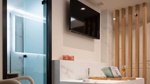 A modern bathroom with a curved sink, a mounted TV, and a wooden partition. - Hanim Boutique |Old Town lux Studio with hot tub 2, Studio (Chania)