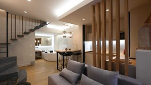 Un salon moderne avec un canapé gris, un escalier et, au fond, un espace cuisine.