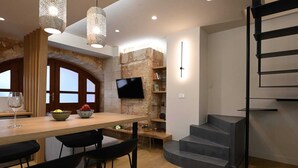 Une cuisine moderne avec une table à manger en bois, des tabourets de bar noirs, un téléviseur fixé à un mur en pierre et un escalier en colimaçon.
