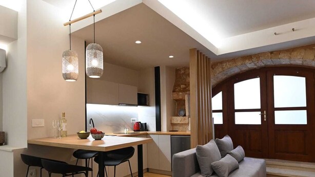 Une cuisine moderne dotée d’un îlot central, de tabourets de bar, de luminaires suspendus et d’un canapé gris, le tout dans un espace de vie spacieux agrémenté d’un plancher en bois.