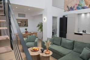 Ein moderner Wohnraum mit Treppe, Essbereich, Küche und einem grünen Sofa mit Obstschale und Vase.