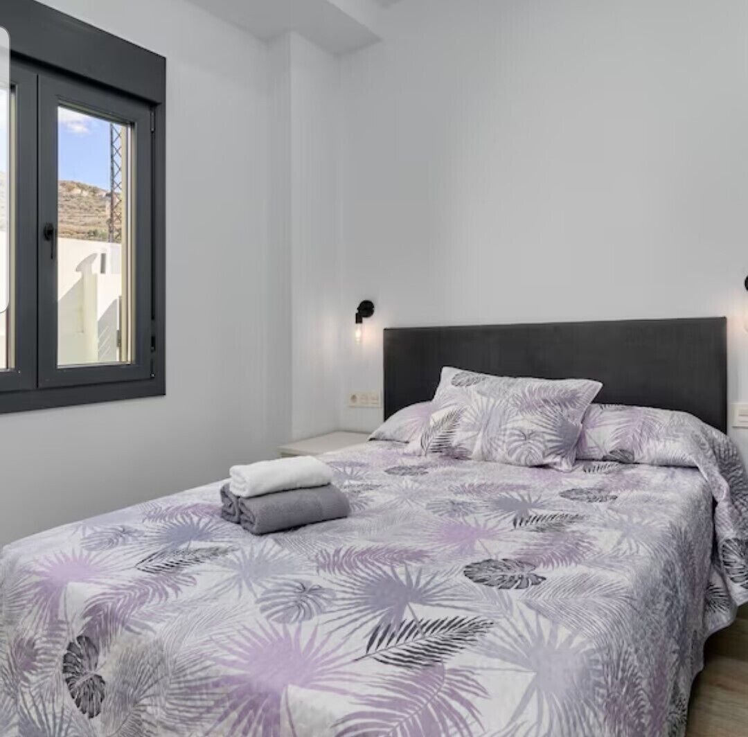 Ein Schlafzimmer mit Bett, Fenster und Wandlampe.