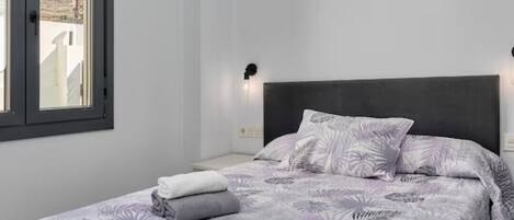 Ein Schlafzimmer mit Bett, Fenster und Wandlampe.