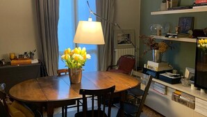 Uma sala de jantar com uma mesa de madeira, cadeiras, um vaso de flores e uma luminária.
