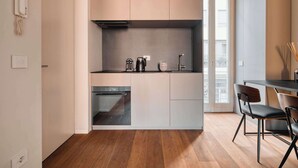 A modern kitchen with a built-in oven, a coffee maker, and a small sink. There is a dining area with a table and chairs. - w Modern 1BR w Balcony in Porta Venezia (Milan)