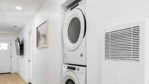 Un lavadero con dos lavadoras apiladas, una rejilla de ventilación, una puerta y un cuadro en la pared.
