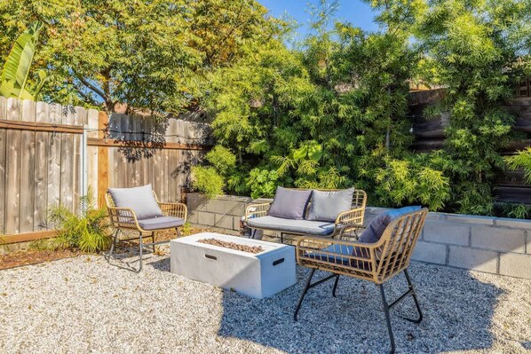 An outdoor seating area with wicker chairs and a concrete table, surrounded by gravel and greenery. - Carlsbad Bungalow Large Backyard (Carlsbad)