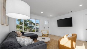 Una sala de estar moderna con un sofá gris, una mesa de centro redonda, una silla de mimbre y una lámpara blanca grande.