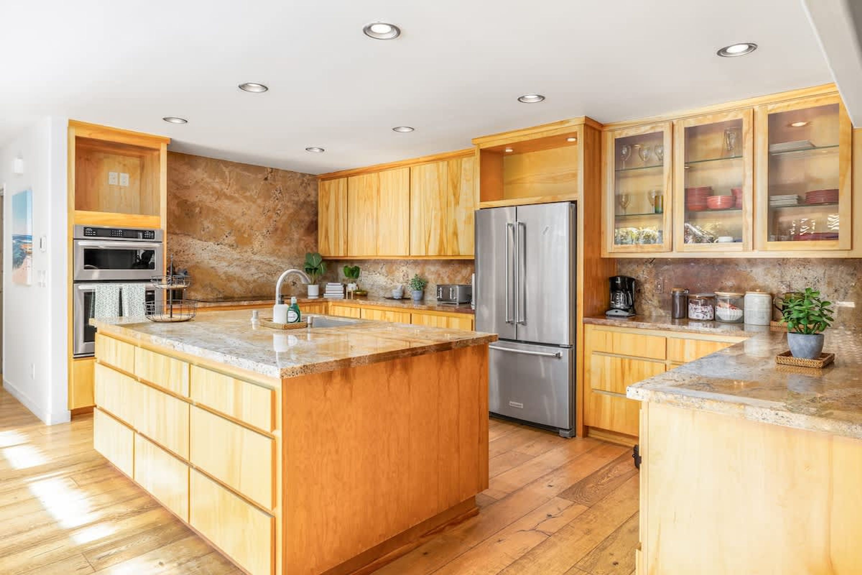 A modern kitchen with wooden cabinets, a stainless steel refrigerator, and a granite countertop.
