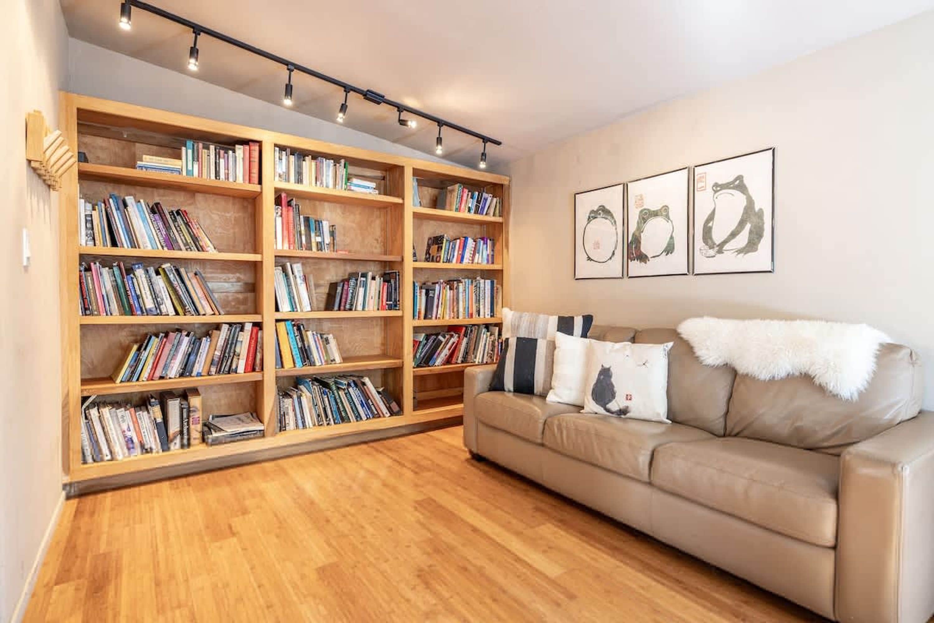 Un salon avec un canapé beige, des étagères en bois et trois reproductions d’œuvres d’art représentant des animaux, encadrées et accrochées au mur.