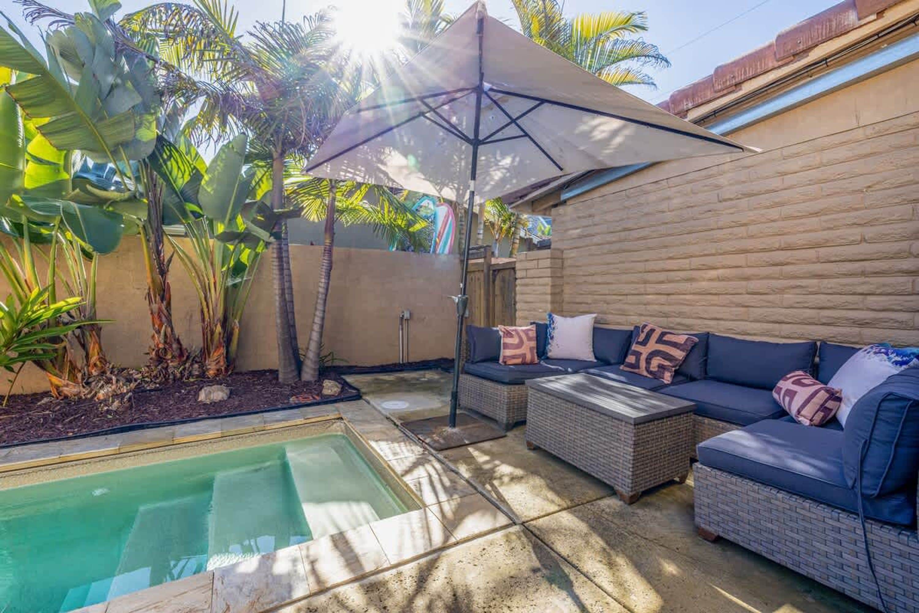 Un área de piscina con un jacuzzi, mobiliario exterior y una sombrilla.