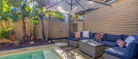 Un área de piscina con un jacuzzi, mobiliario exterior y una sombrilla.