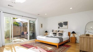 A bedroom with a bed, a wooden floor, a red rug, a wooden cabinet, and a wall with a framed picture. - Carlsbad Zen - Large Pool (Carlsbad)