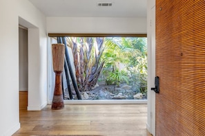 A modern interior with a wooden floor, a large window with a view of tropical plants, and a tall decorative column. - Carlsbad Zen - Large Pool (Carlsbad)