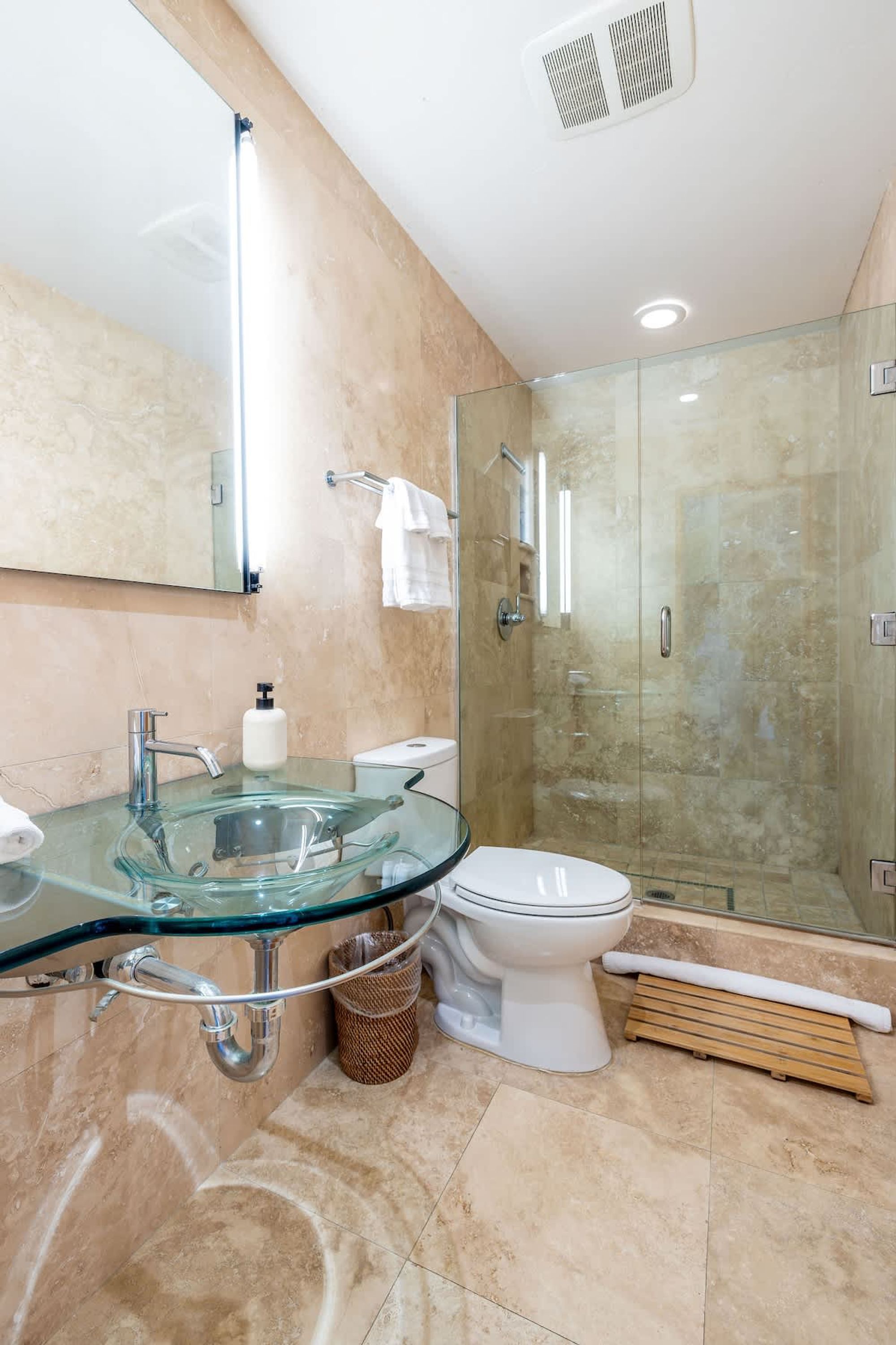 A modern bathroom with a glass sink, a toilet, and a glass-enclosed shower area.
