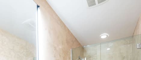 A modern bathroom with a glass sink, a toilet, and a glass-enclosed shower area.