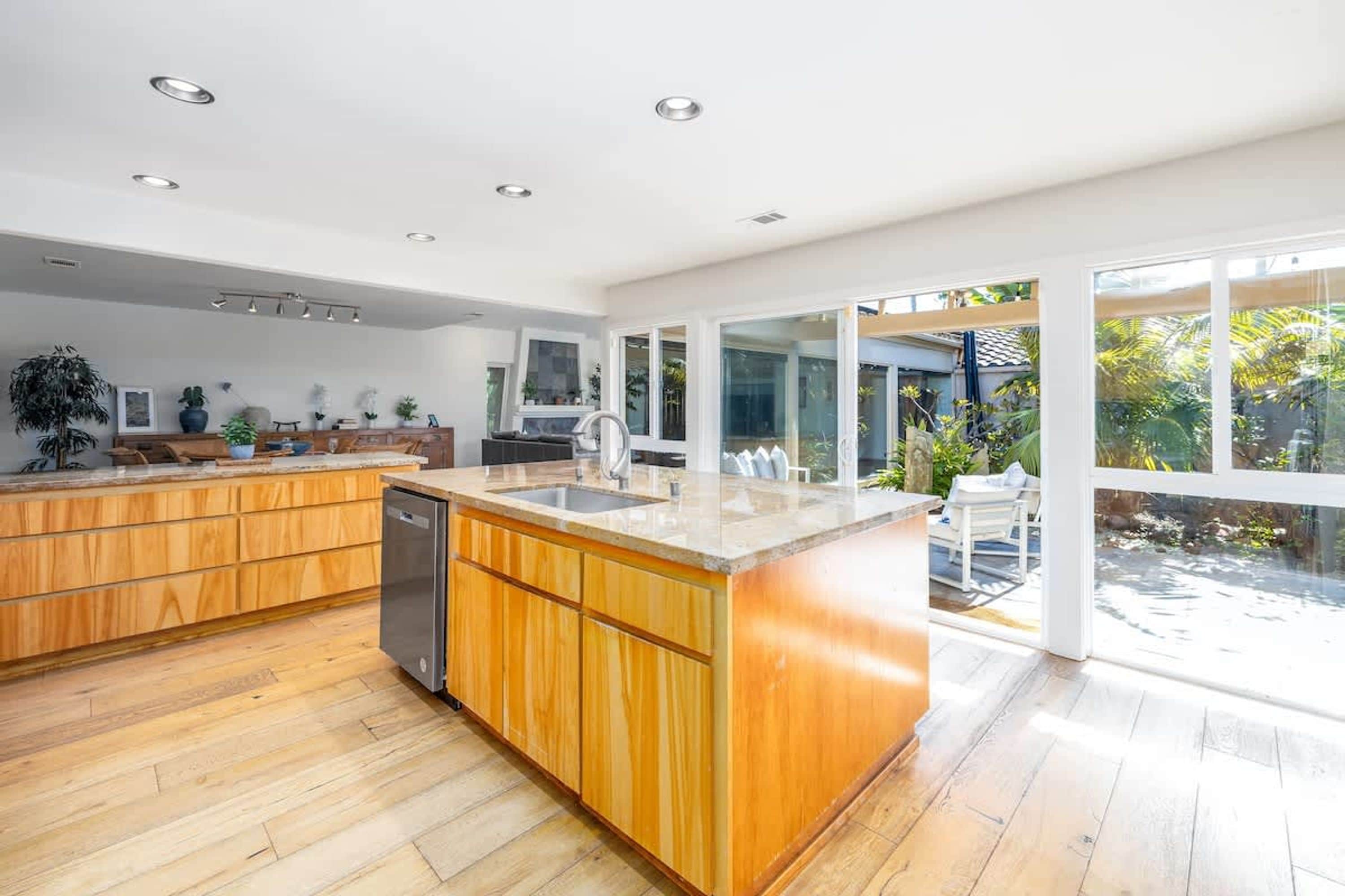 Een moderne keuken met houten kastjes, een centraal eiland en een groot raam met uitzicht op de omgeving.