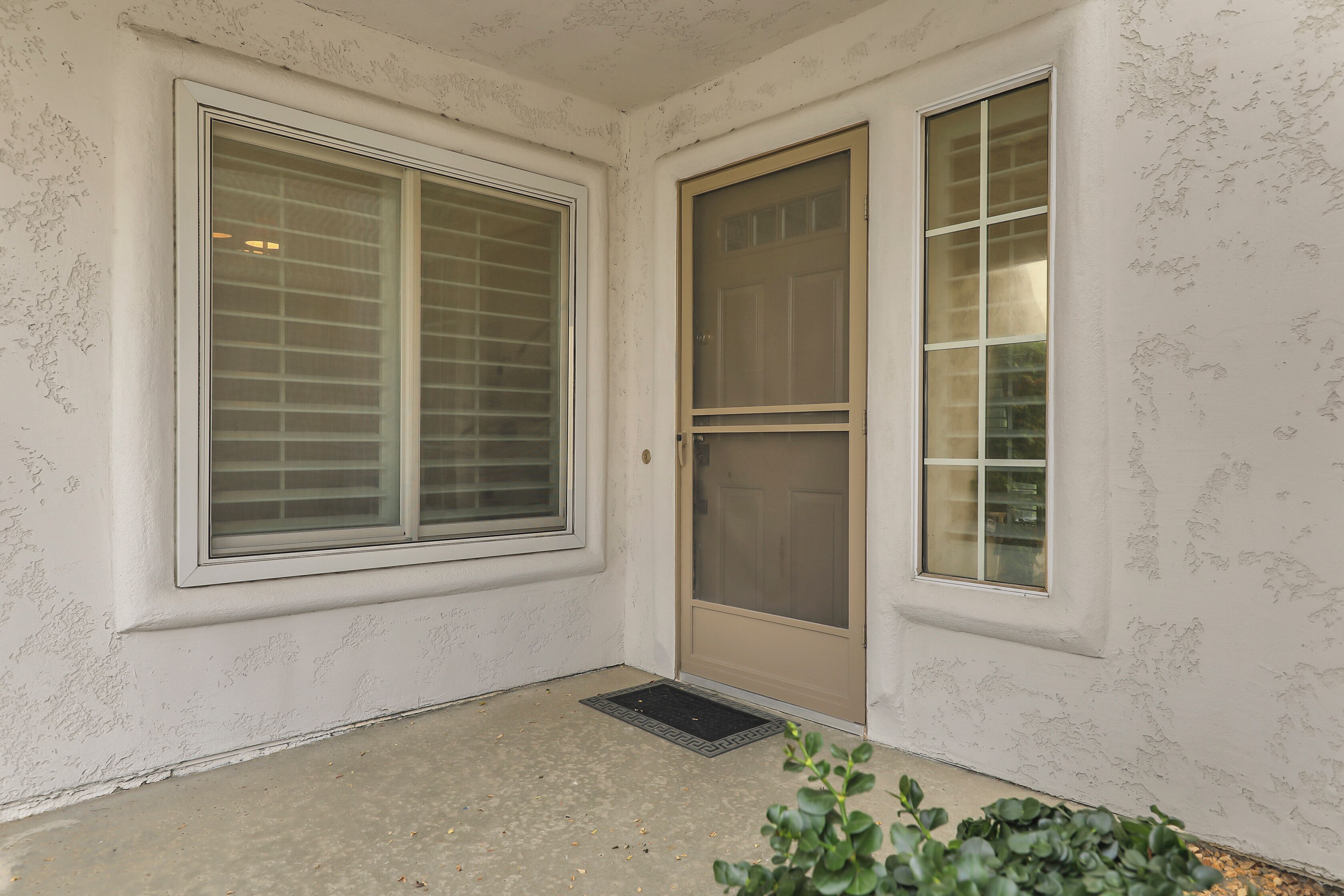 A corner of a room with a large window, a door with a screen, and a small mat on the floor.
