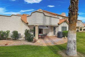 Una casa con patio, una zona salotto coperta all'aperto e una palma.