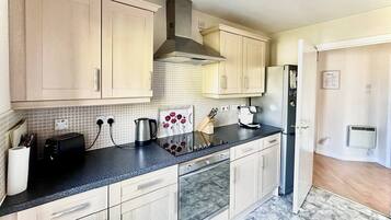 A modern kitchen with light wood cabinets, a stainless steel range hood, a coffee maker, and a refrigerator.