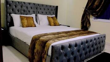 Cama com cabeceira estofada, roupa de cama branca e duas almofadas decorativas.