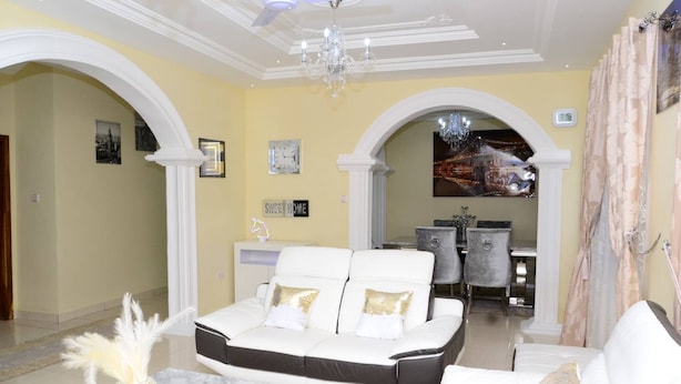 A spacious living area with a white sofa set, a chandelier, and a dining area in the background. - Janhas Senegambia Villa Rental 3 With Free Wi-fi (Serrekunda)