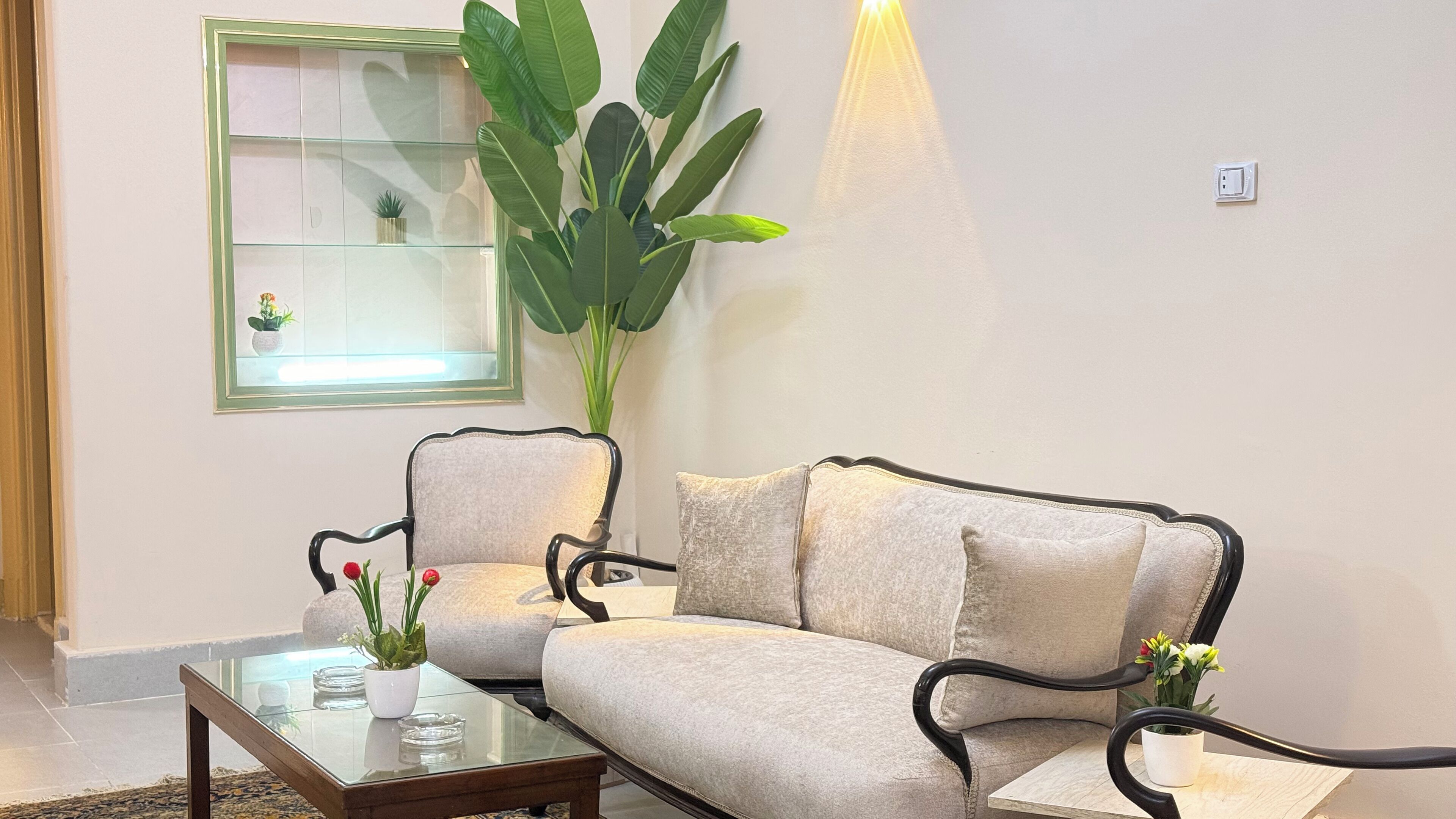 A living room with a sofa, two armchairs, a glass coffee table, and a large potted plant.