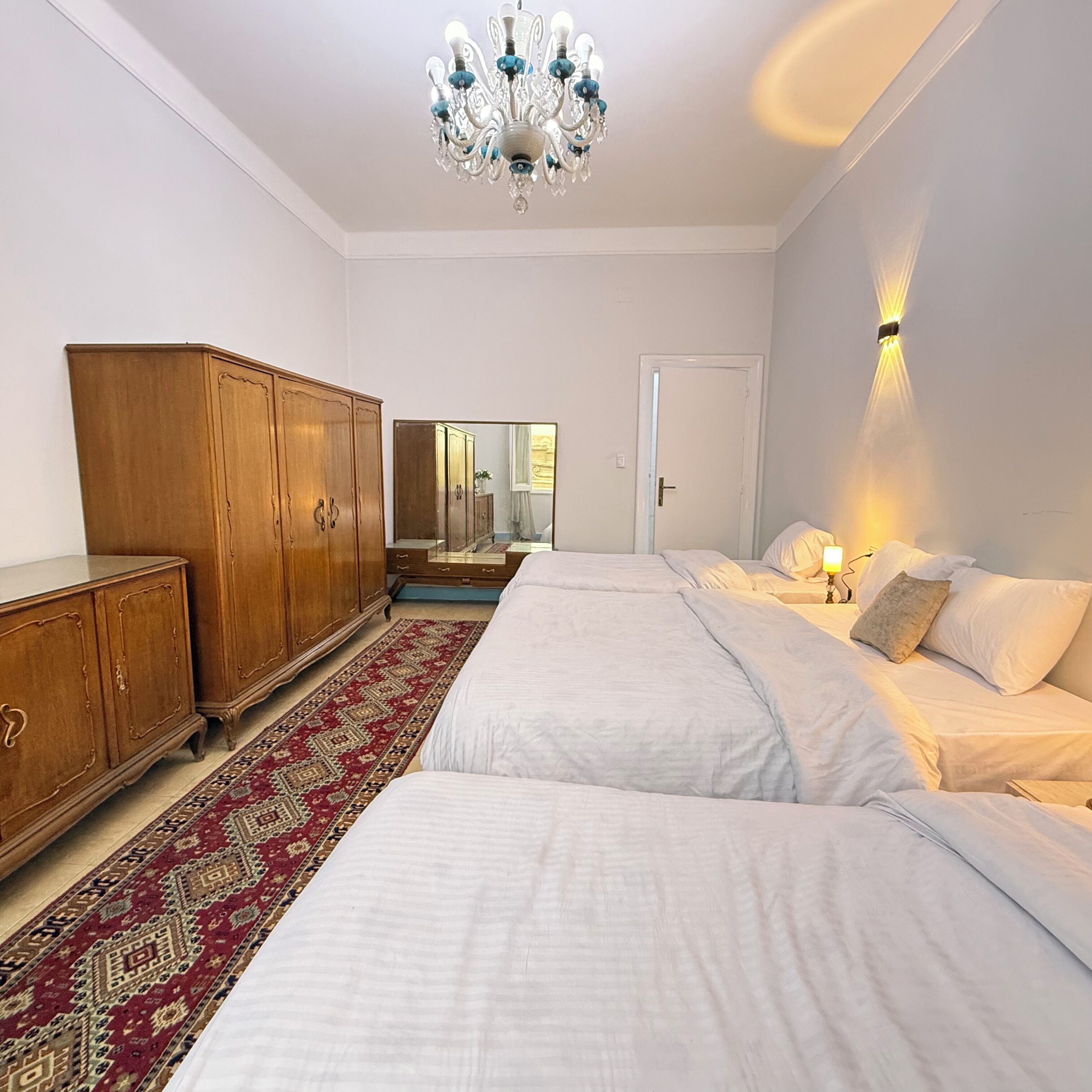 A bedroom with a large bed, a wooden wardrobe, a mirror, and a chandelier.