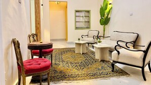 A room with a round table, a red upholstered chair, a sofa, and a large plant. - Palace View Royal Home (Cairo)