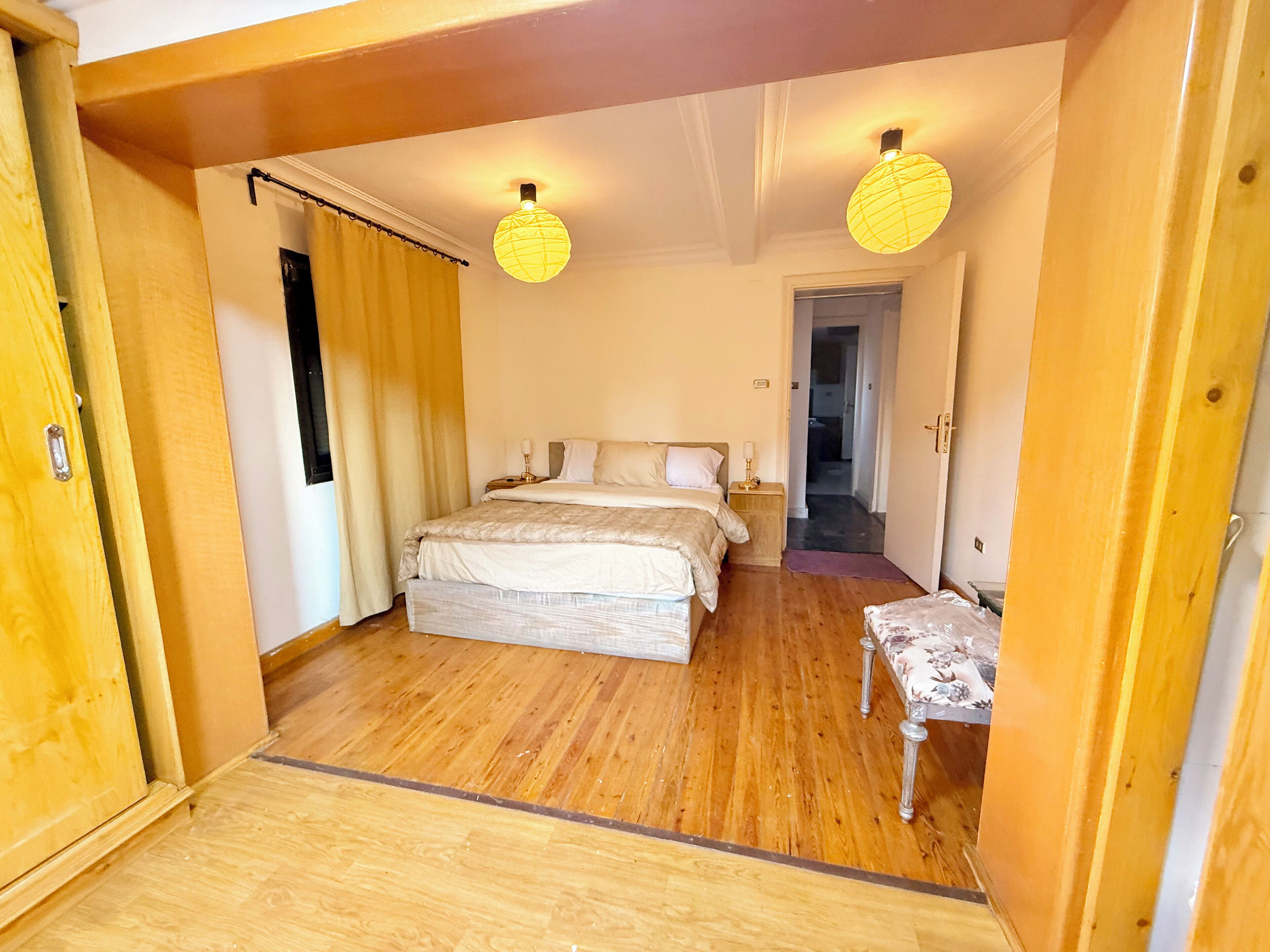 A bedroom with a large bed, wooden flooring, and two hanging lamps.