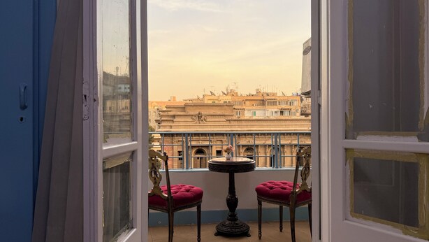 A balcony with a table and two chairs, overlooking a historic building with arches and a balcony. - Palace View Royal Home (Cairo)