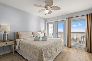 A bedroom with a large bed, a ceiling fan, a nightstand, a lamp, and a view of the outside. - Beachfront Townhome! GO-JO Getaway! Coastal Comfort, 2BR Sleeps 6 (Panama City Beach)