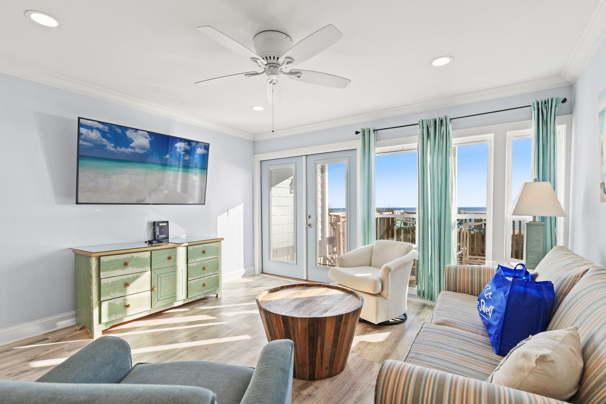 A spacious living room with a large window, a ceiling fan, a green cabinet, a striped sofa, and a coffee table.