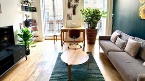 A living room with a sofa, a TV, a coffee table, a dining table with chairs, and a large window. - Flat 1 Modern Marylebone Apartment with Balcony (London)
