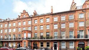 A row of red brick townhouses with multiple windows and balconies, featuring a classic architectural style. - Flat 1 Modern Marylebone Apartment with Balcony (London)