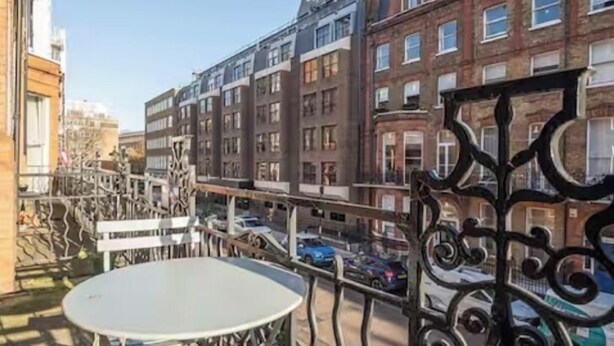 A balcony with a round table and chairs, overlooking a street with parked cars and buildings. - Flat 1 Modern Marylebone Apartment with Balcony (London)