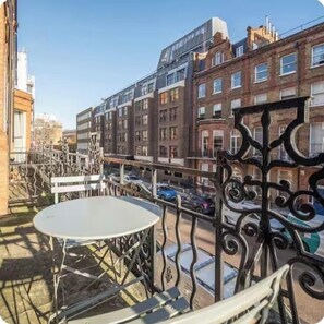 A balcony with a round table and chairs, overlooking a street with parked cars and buildings. - Flat 1 Modern Marylebone Apartment with Balcony (London)