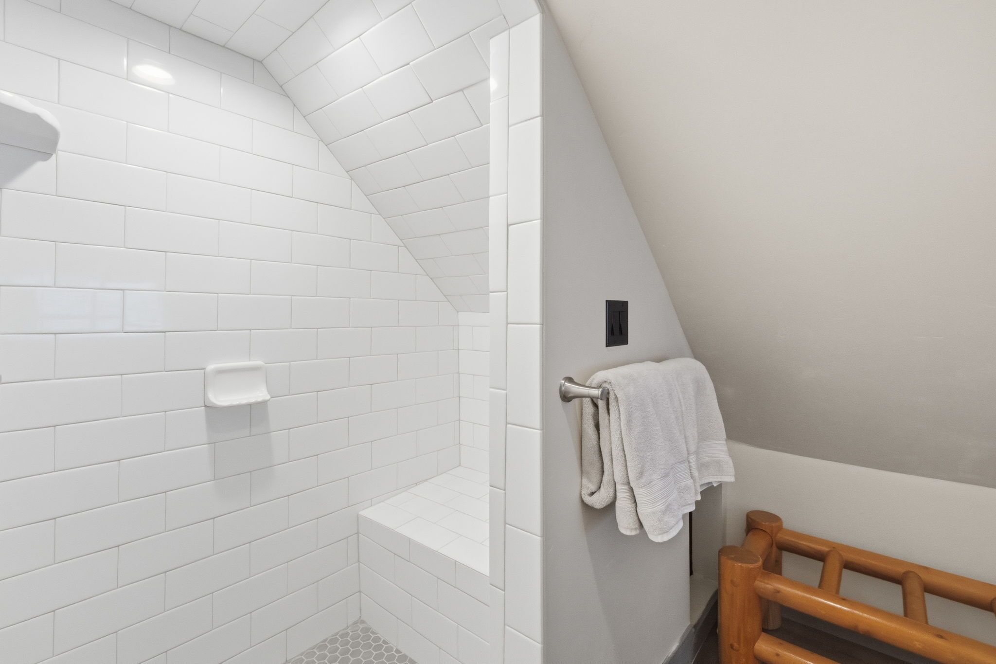 Ein modernes Badezimmer mit weißen Fliesen, einer Duschkabine, einer Holzbank und einem Handtuchhalter.