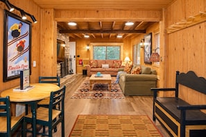 A cozy cabin interior with a wooden interior, a dining area with a table and chairs, a sofa, and a patterned rug. - Creekside Cabin by Cottonwood Lodging (Brighton)